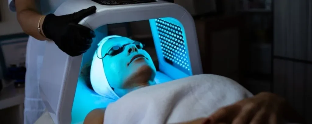 `Paciente recibiendo terapia de luz LED azul facial en clínica estética`