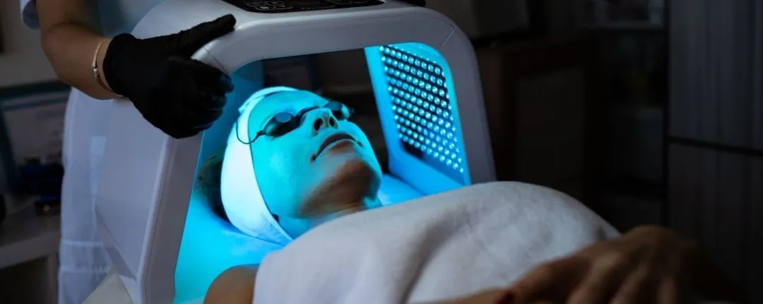 `Paciente recibiendo terapia de luz LED azul facial en clínica estética`